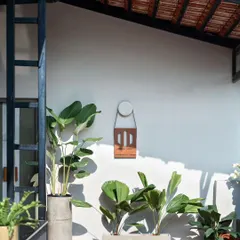 A view of the office entrance showing the custom corten steel signage with a leather strap. The combination of rustic steel, terracotta floor tiles, and lush plants creates a rich textural palette that feels warm and grounded.