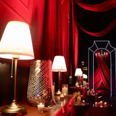 A detailed view of the decor, with warm table lamps, pearl strings, and mosaic vases set against dramatic red draping.