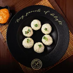 "Tiny parcels of delight." Six perfectly formed dumplings are presented on a textured black plate, showcasing the meticulous craft that goes into each bite-sized creation.
