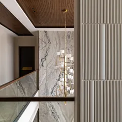 A detail shot looking up the stairwell, highlighting the rich texture of the fluted wall panels, the warm wood ceiling, and the dramatic marble wall that serves as a backdrop for a cascading chandelier.