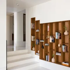 This recessed bookcase is designed to follow the staggered floors of the home. The asymmetrical shelves create a dynamic display for books and objects, turning a simple wall into a piece of functional art.