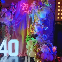 "Stay Sassy" at 40! This glamorous 40th birthday backdrop combines a neon sign, light-up numbers, and a beautiful arrangement of balloons and flowers for a truly fabulous celebration.