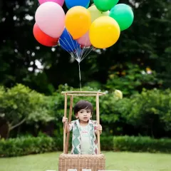 Up, up, and away! This hot-air balloon prop is a client favorite for first birthday shoots, creating a joyful and adventurous portrait against a beautiful outdoor backdrop in a Mumbai park.