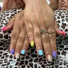 A playful and vibrant multi-color manicure. Each nail is painted with a different pastel shade, including neon yellow, lavender, and sky blue, with glitter accents for a fun and eye-catching result.