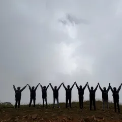 The silhouette of our trekking group against the cloudy sky at Kudremukha peak, holding hands in celebration of reaching the summit.