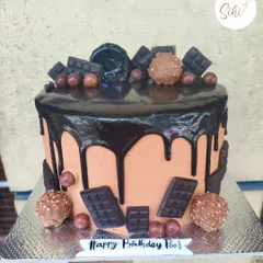 A classic chocolate overload cake. This decadent creation features a rich chocolate drip, topped with Ferrero Rocher chocolates and various chocolate bars.