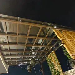 A glass pergola seen at night, with ambient string lights creating a warm and inviting atmosphere. This project at Swiss Town, Bangalore, combines a metal frame with a bamboo privacy screen for a rustic-modern look.