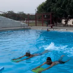 Two students practice their flutter kicks side by side using kickboards, building confidence and endurance in the water during a lesson.