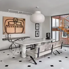A modern and artistic dining space featuring a marble table with sculptural legs, a custom bench, and bold artwork. The black and white marble floor adds a classic touch to the contemporary setting.