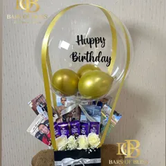 A hot air balloon-themed hamper perfect for a loved one's birthday. It features a box of white roses and chocolates, with a photo collage rising up into a balloon display.
