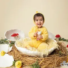 A happy little chickadee in her nest. This Easter-themed shoot is full of whimsy and charm, with a bright yellow outfit and cute props that celebrate the season.