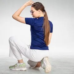 A model in a navy blue t-shirt and white pants in a dynamic pose, demonstrating flexibility and style for a sportswear brand.
