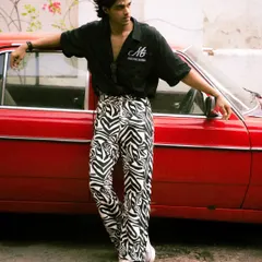 A bold fashion statement against a vintage red car. The contrast between the car's color and the model's zebra-print pants creates a visually striking urban portrait.
