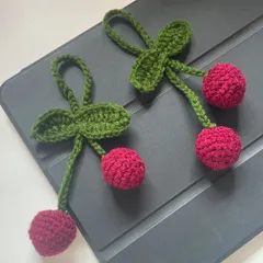A pair of sweet cherry bag charms. Hand-crocheted with bright red yarn, these are perfect for adding a touch of retro fun to your accessories.