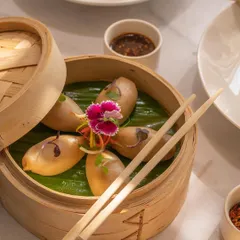 Styling for a plate of dim sum, presented in a traditional bamboo steamer. The composition uses chopsticks to create leading lines, drawing the viewer's eye to the artfully arranged dumplings.