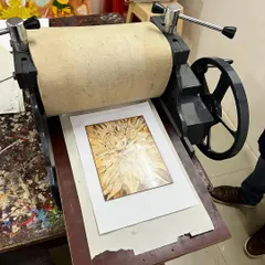 The moment of truth. A woodcut block of a sunflower is carefully placed on the printing press, ready to be inked and transferred onto paper.