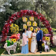 The happy family-to-be posing in front of a stunning floral arch of sunflowers and red bougainvillea, complete with cute cutouts of their dogs.