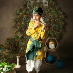 A boy dressed as Lord Krishna stands proudly playing a flute, with a backdrop of peacock feathers creating a divine atmosphere.