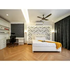 A bedroom that combines crisp white bedding with a bold, geometric accent wall. The herringbone wood flooring adds warmth and texture, while the integrated desk and shelving create a functional and stylish workspace.