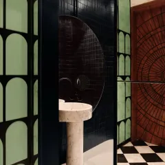 The attached bathroom in the entertainment den continues the bold theme with a striking pedestal marble sink, black-and-white checkered flooring, and a uniquely carved wooden door.