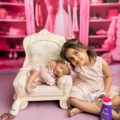 A new big sister gently cuddles her newborn sibling in a whimsical, pink-themed princess closet setup.
