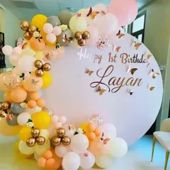 A 'Happy 1st Birthday' backdrop with a custom printed circular panel and a balloon garland in pastel yellow, orange, and grey.