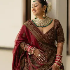 A candid portrait of the bride, Anjani, sharing a moment of pure laughter. Her stunning green and gold jewelry and traditional attire are beautifully captured.