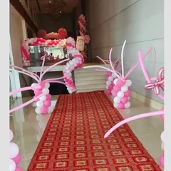 A grand hallway entrance decorated with pink and white balloon arches and columns. The red carpet leads guests into the main event space in style.