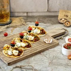 These mini naan pizzas were shot to look like the perfect shareable appetizer. The composition on the wooden board with fresh ingredients scattered around gives a relaxed, social vibe, ideal for a cafe or bar menu.
