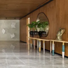 The vast entrance lobby of the K Residence, featuring a console with uniquely crafted monolithic marble legs. The space is designed to be an art gallery, with a contemporary brass mirror reflecting an installation on the opposite wall.
