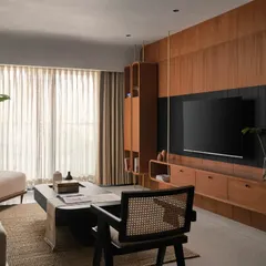 The living room is designed for both relaxation and entertainment, with a custom teak wood veneer TV unit that features integrated shelving. The clean lines and natural materials keep the space feeling open and uncluttered.