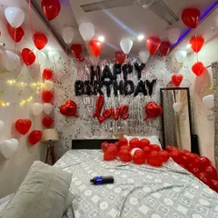 This is a wide view of a popular romantic birthday setup I offer. I cover the ceiling with red and white balloons, create a feature wall with a silver fringe curtain and bold 'Happy Birthday' lettering, and scatter more balloons on the bed to complete the immersive surprise experience.