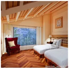A twin bedroom in a mountain resort, designed to maximize comfort and views. The room features herringbone wood flooring, a large picture window framing the landscape, and warm, ambient lighting for a cozy feel.