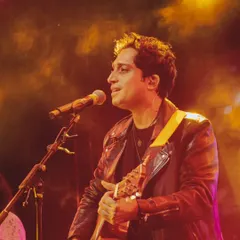 A close-up, atmospheric shot of Nikhil D'Souza performing under warm stage lights.