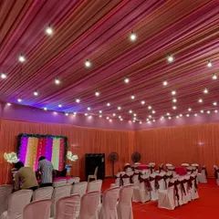 We designed this indoor space for a Mehendi ceremony with a warm and inviting pastel theme. The ceiling is draped in pink and orange fabric with hanging bulbs, complementing the colorful stage backdrop and elegant guest seating.