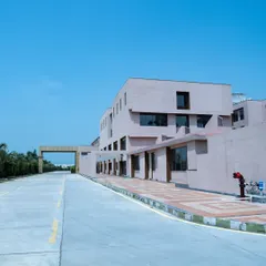A long-range view of the Konark Academy campus, showing the main road leading to the entrance. The building's soft beige facade stands out against the clear blue sky, presenting a clean and inviting image.