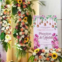 The welcome signage for the 'Phoolon ki Haldi', featuring bright floral graphics and traditional temple bells. This set a festive and welcoming tone for the event right from the entrance.