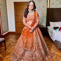 A full view of Shikha's stunning orange lehenga. The makeup was designed to create a royal glow, with a luminous base and soft eye makeup that balanced the vibrant color of her outfit.