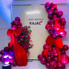 A bold and romantic birthday decoration in shades of red and magenta. The white arched backdrop is personalized and framed with a dramatic balloon arrangement and large red bows.