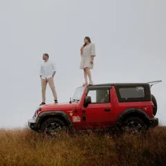 A powerful shot of a couple on their jeep against a stark, open landscape, showcasing a sense of freedom and shared adventure.