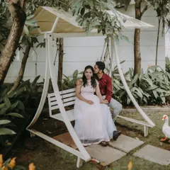 A romantic moment on a garden swing at a resort. The lush greenery and gentle kiss create a fairytale scene.