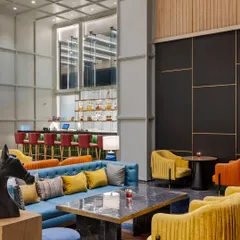 The main lounge area at Holiday Inn, Lucknow, is designed for comfort and social engagement. A mix of vibrant blue, yellow, and orange seating is arranged to create multiple conversation zones, unified by a large, colorful area rug.