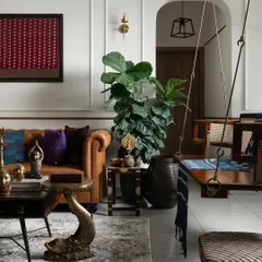 I love creating spaces that feel layered with history and personality. This living room corner features a classic tan leather sofa, a traditional wooden swing, and unique brass decor like the fish-shaped table. It’s a celebration of Indian craft and modern comfort, all in one frame.