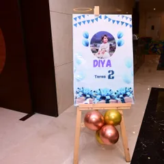 This welcome board for a second birthday party features a simple and clean design. It includes the child's photo and is accented with metallic balloons.
