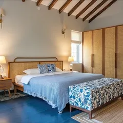This bedroom in our Goa villa project embraces rustic charm with a modern touch. The custom bed features a natural rattan headboard, paired with oak side tables and a vibrant floral bench. The exposed wooden ceiling beams add to the room's character.