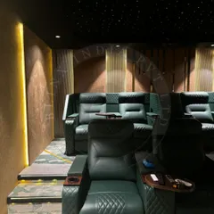 Luxury is in the details. This view highlights the custom diamond-stitched green leather recliners, each equipped with a personal tray table and cupholder. The fiber optic starfield ceiling above adds a touch of magic, simulating a night sky for an unforgettable movie night.