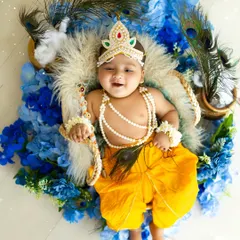 An adorable overhead shot of a baby in a Krishna outfit, lying on a bed of blue flowers and peacock feathers. His sweet smile makes this photo extra special.