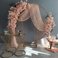 An example of a romantic and elegant setup, perfect for an engagement or anniversary. It features a gold ring frame with pink cherry blossoms, sheer draping, and fairy lights.