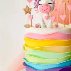 A vibrant and cheerful unicorn cake with rainbow-colored ruffled buttercream layers. It's topped with a happy unicorn figurine, stars, and hearts.