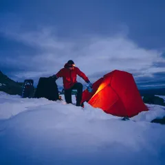 Setting up camp as the last light of day fades over a snow-covered landscape. This is a moment of preparation and anticipation for a quiet, cold night in the mountains.